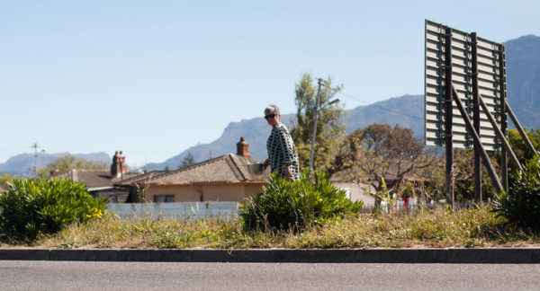Woman standing on open field with urban house settlement in the background.